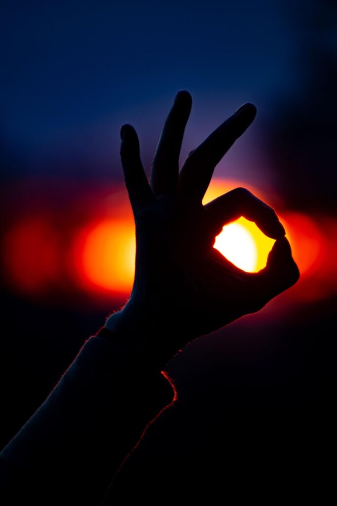 hand showing "ok" or "no problem" gesture with bright light behind