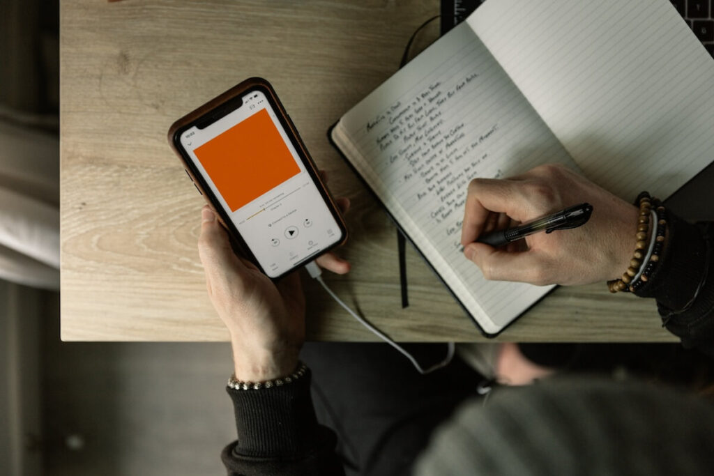 person writing down notes while listening to a podcast on phone