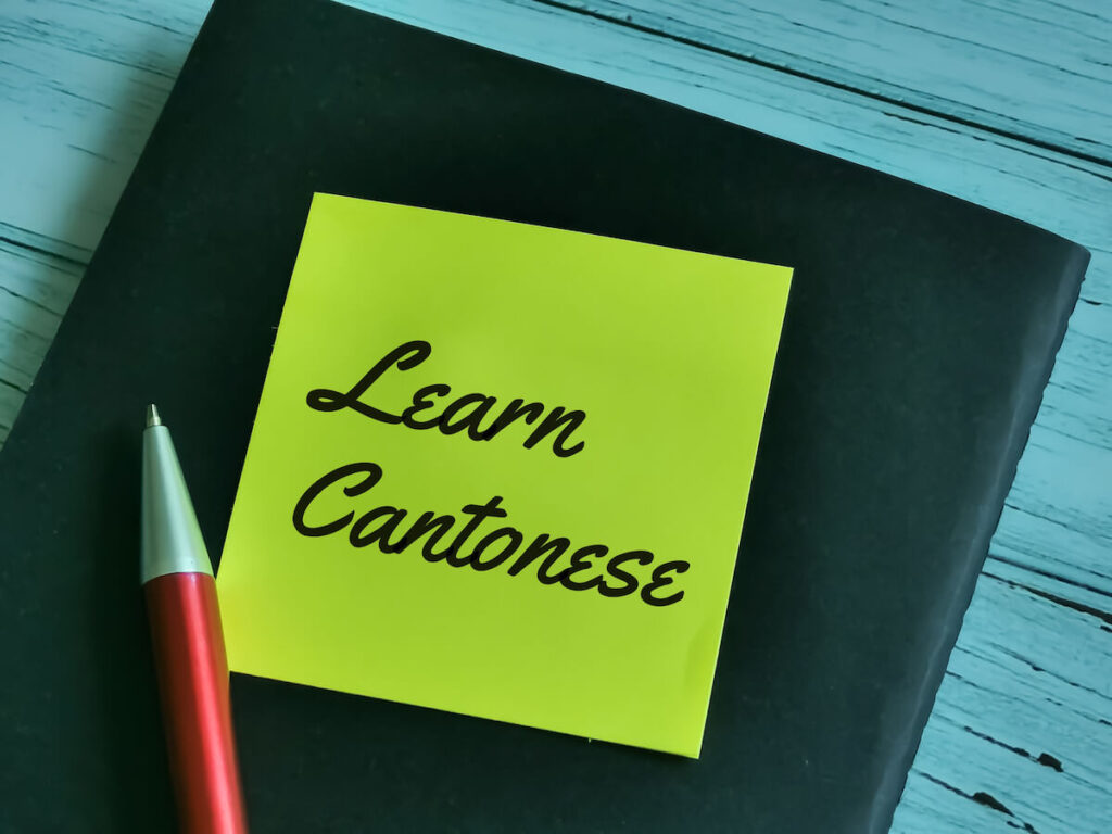 Phrase learn Cantonese written on sticky note with a pen and book