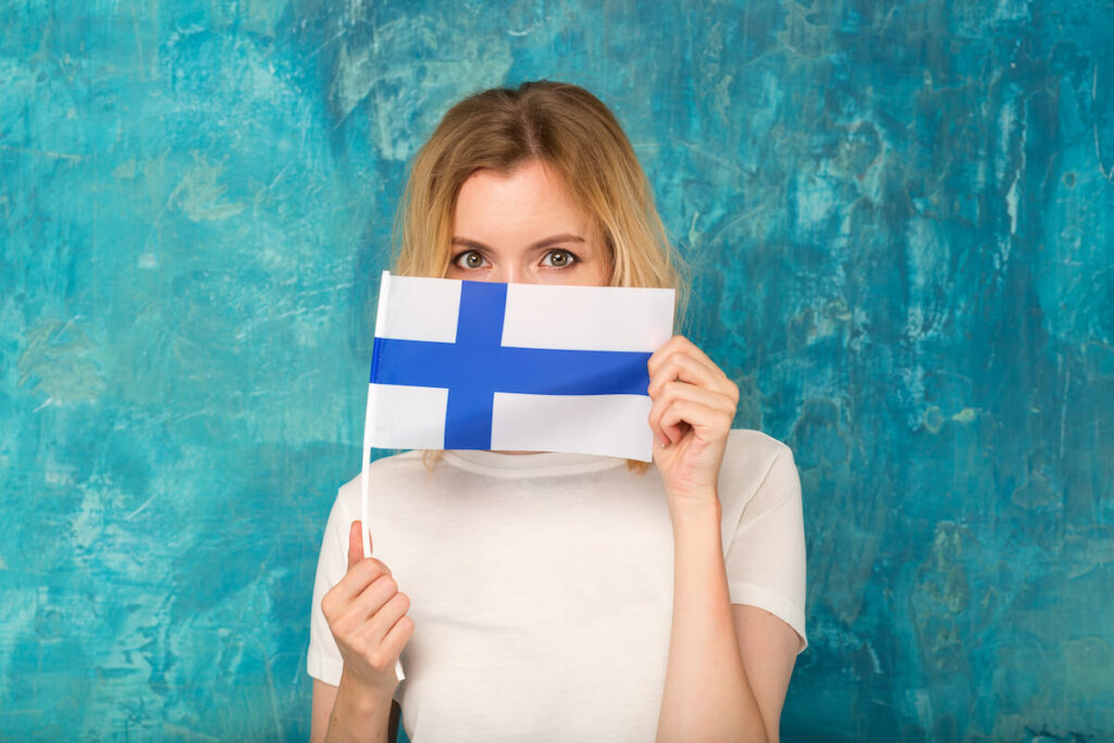 woman covers her face with the flag of Finland standing on a blue background