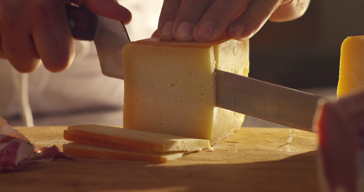 chef-cutting-cheese-with-a-knife on-wooden-board chef cutting cheese with a knife on wooden board