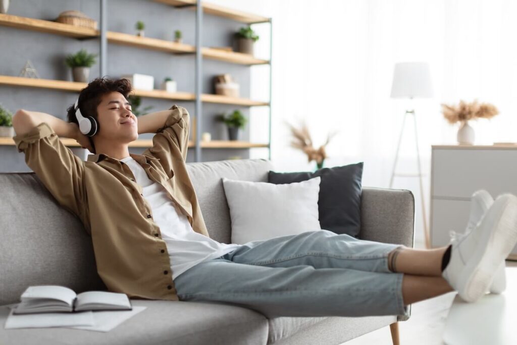Calm asian man sitting on couch, listening to music