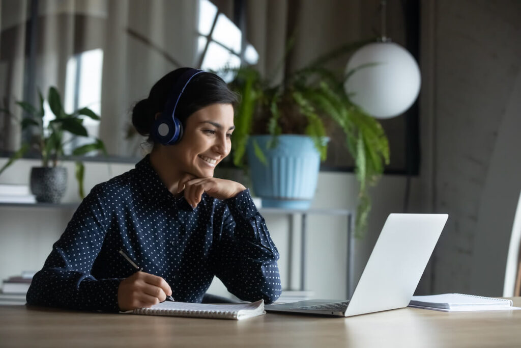 Happy young woman with wireless headphones looking at laptop screen
