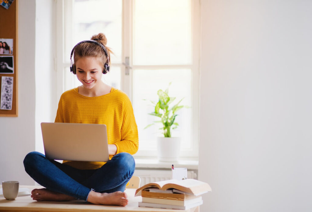 A young female student sitting at the table, using headphones when studying