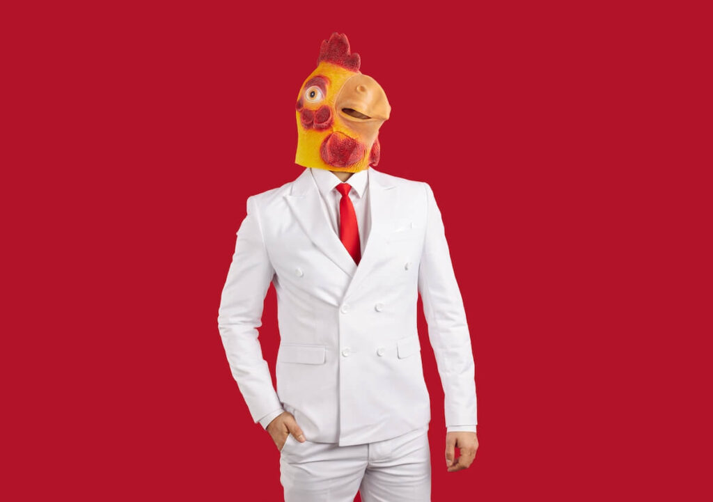 man wearing elegant white suit and silly freaky yellow masquerade chicken mask