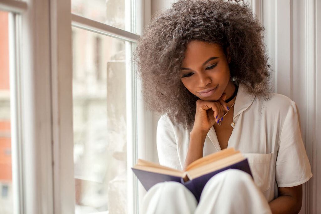 woman reading a book sitting on the windowsill