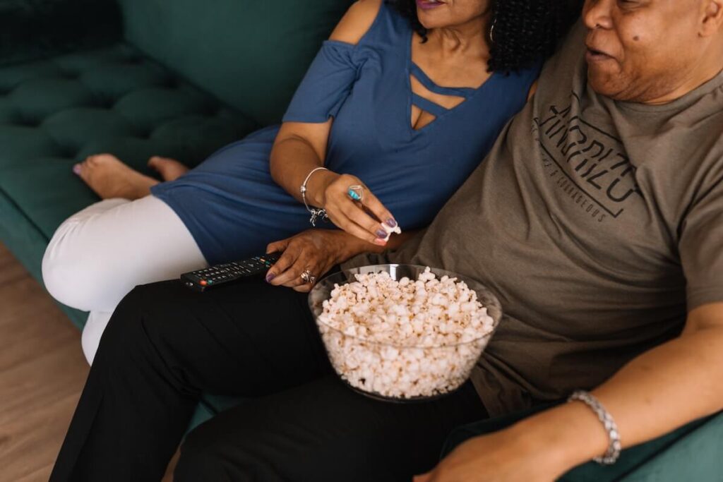 couple sitting on a green couch watching tv and eating popcorn