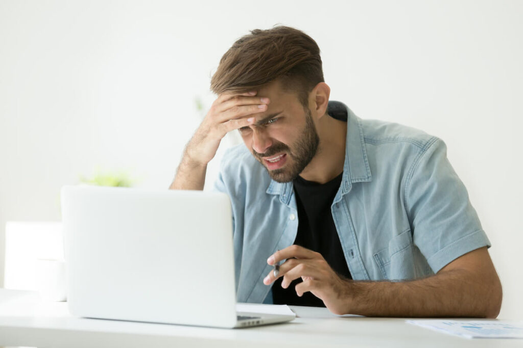 Confused young man frustrated by online problem looking at laptop screen
