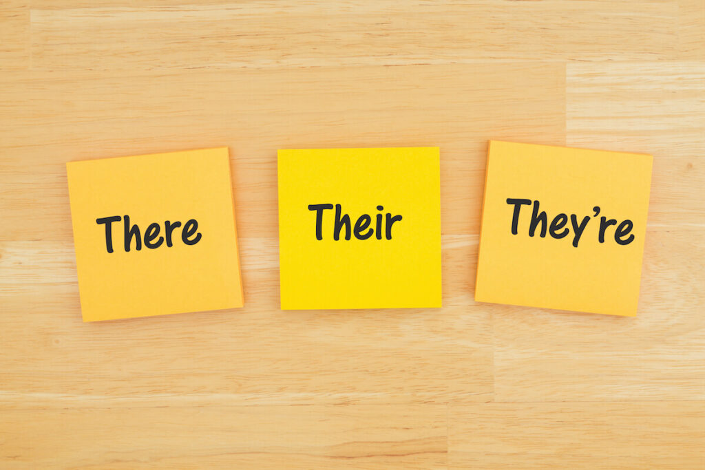 Grammar of there, their, they're on three sticky notes on textured desk wood