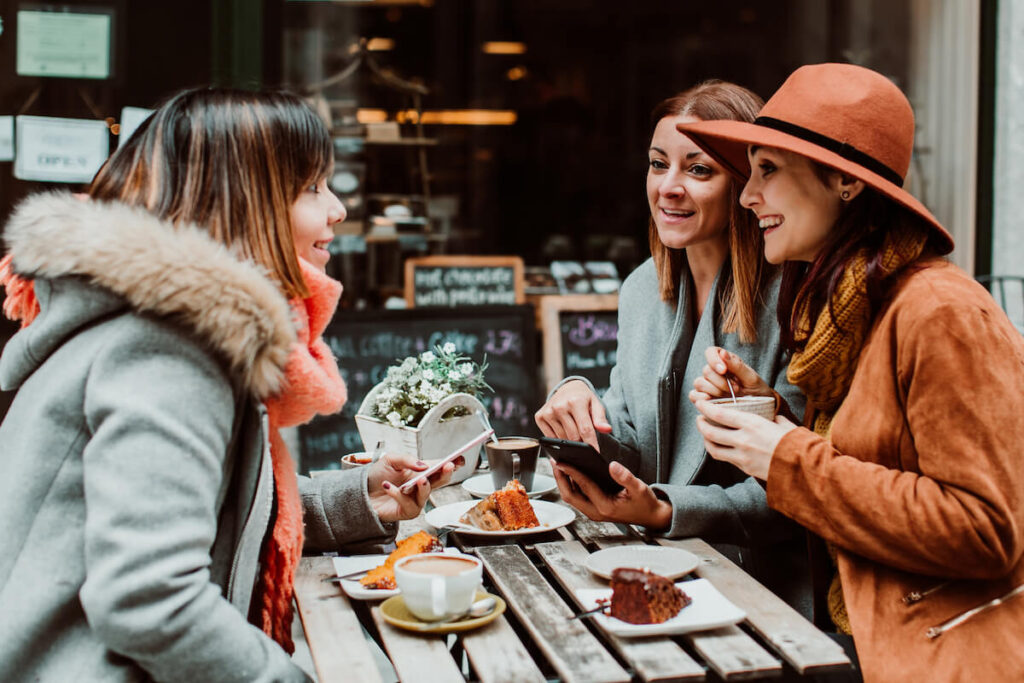 Group of young friends drinking coffee with cakes in an outdoor cafe in Porto, Portugal