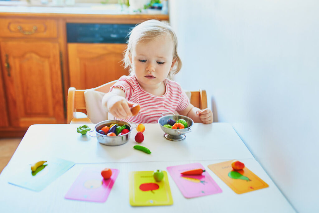 Adorable little girl playing with toy fruits and vegetables at home, in kindergaten or preschool