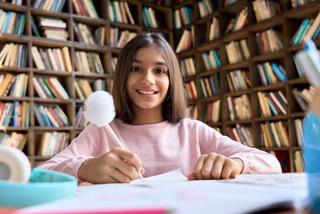Happy smiling girl sitting at table learning at home classroom, having online video call