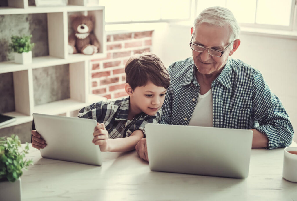 grandpa and grandson are using gadgets and smiling while spending time together at home
