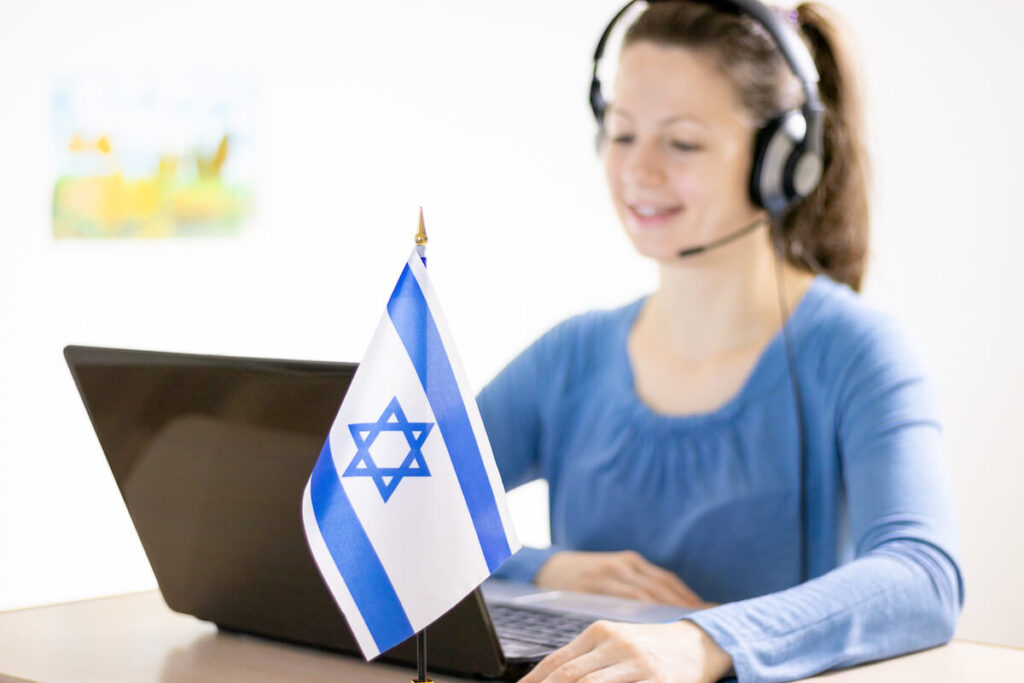 girl sitting in front of a laptop with a Israeli flag on the table and communicating on a computer using a headset