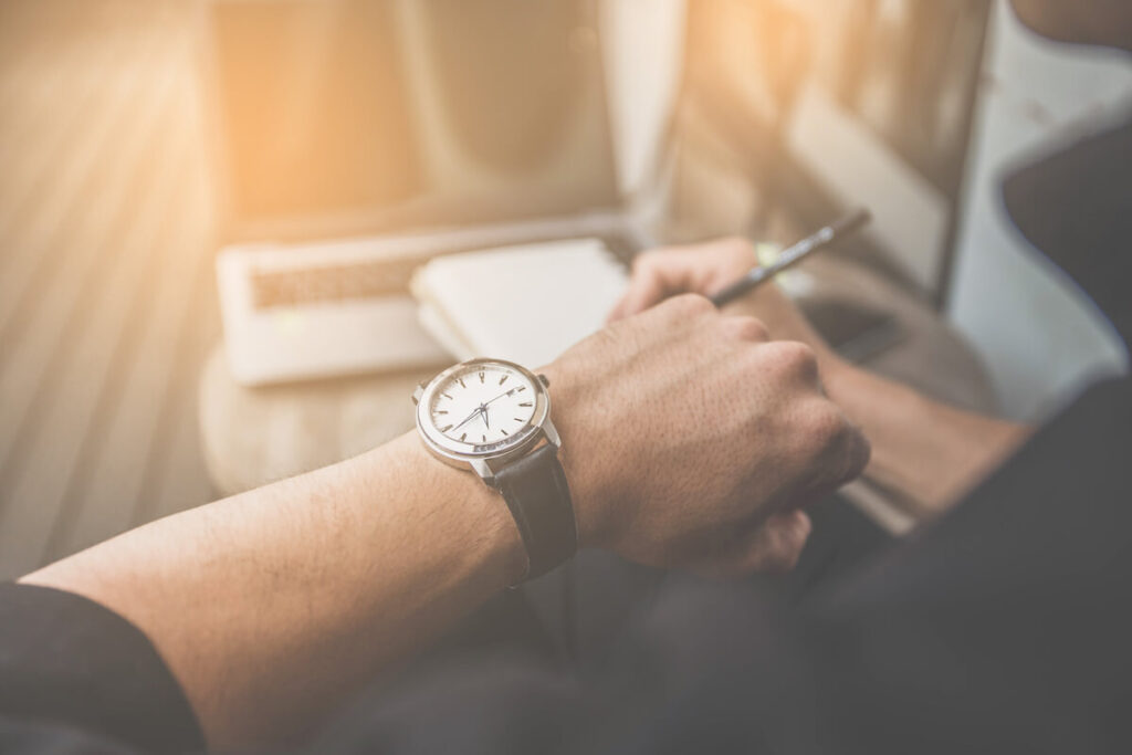 soft focus businessman looking at his watch on his hand, watching the time and writing something on note book