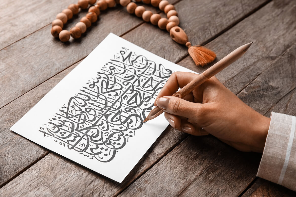 Arabic calligraphist writing on paper sheet against wooden background