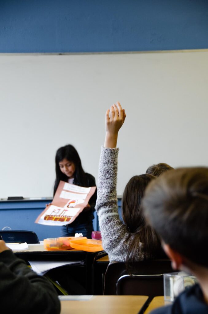kid raises hand as another presents in class