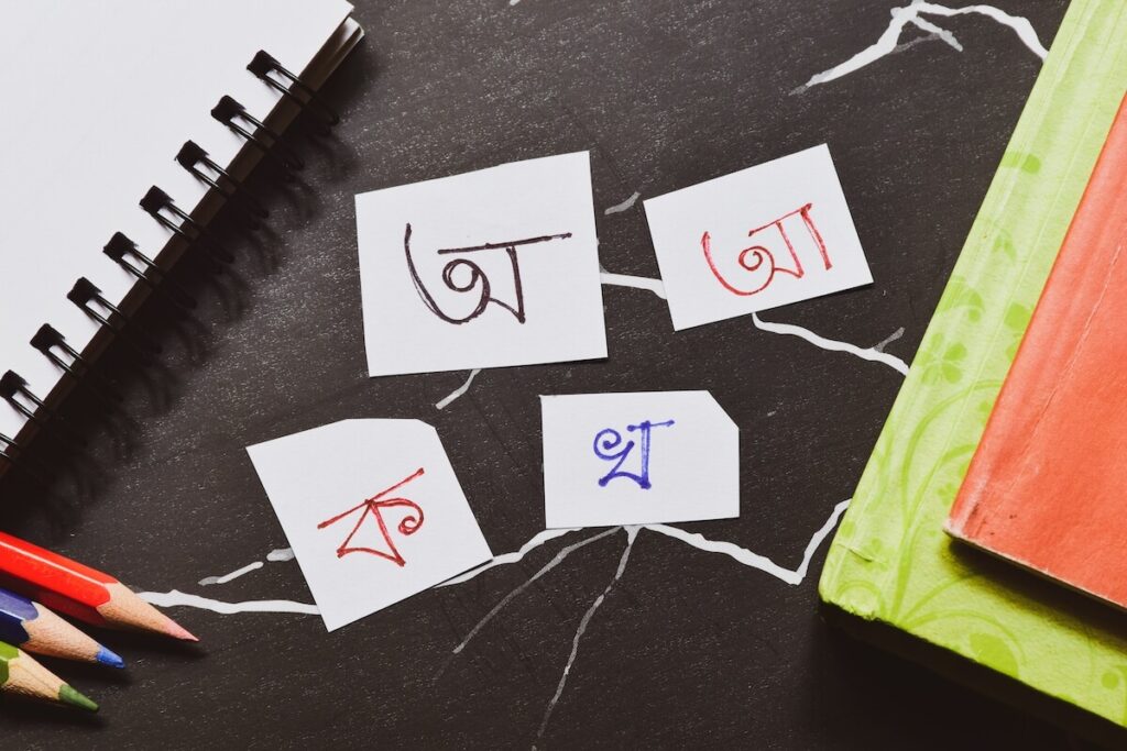 Bengali alphabet handwritten on piece of papers on study table with notebooks