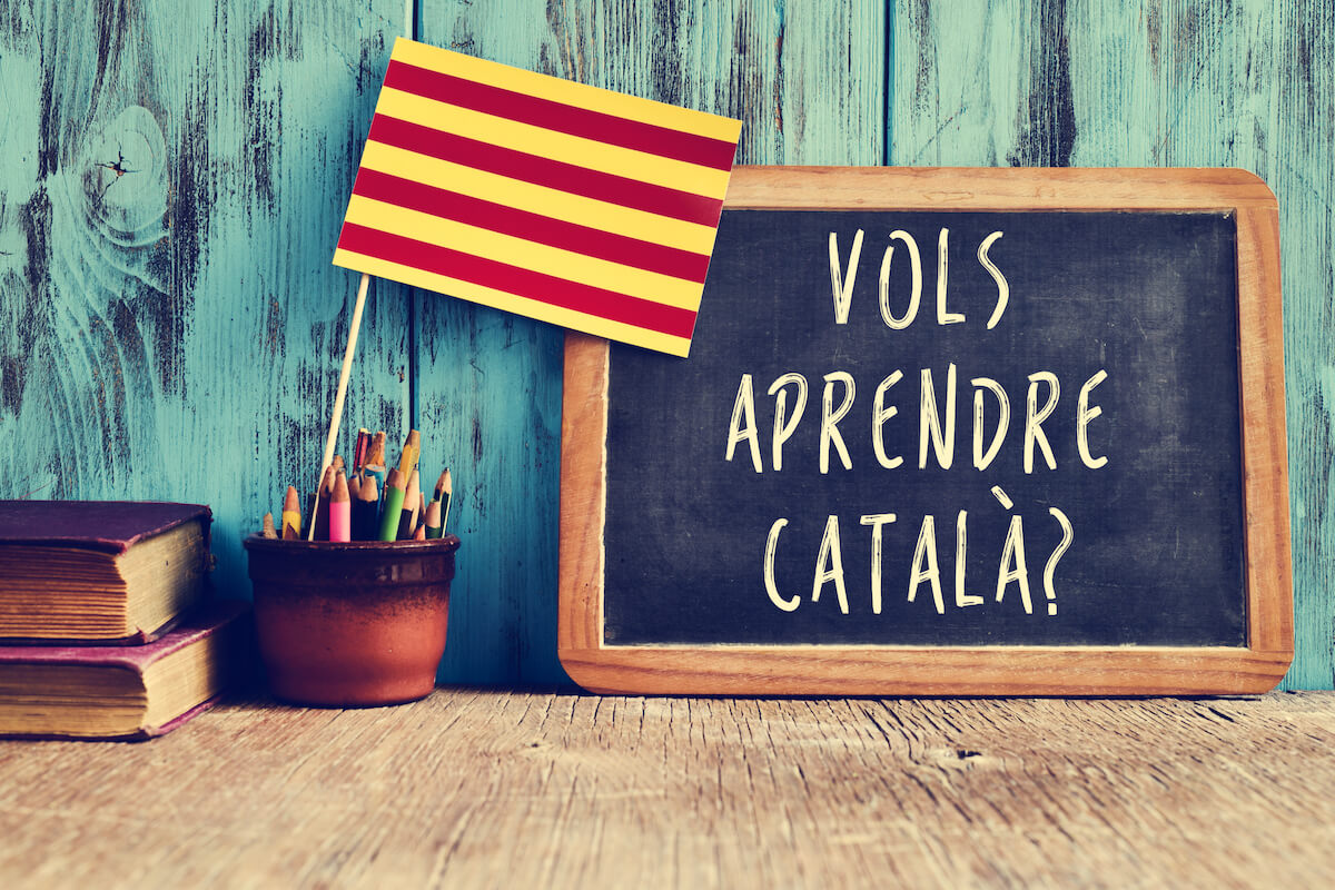 a flag of Catalonia and a chalkboard with the question "vols aprendre catala?"