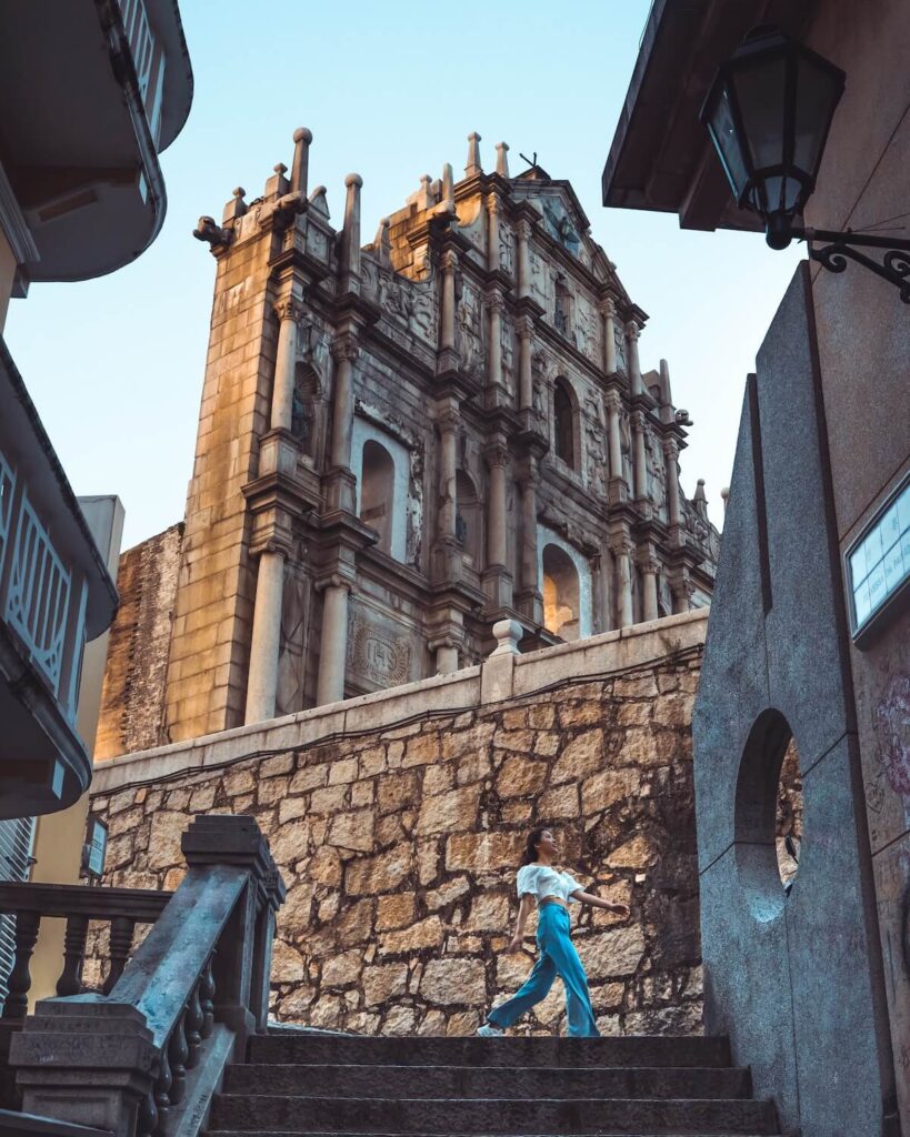 girl in blue jacket and blue denim jeans walking near brown concrete building in Macau