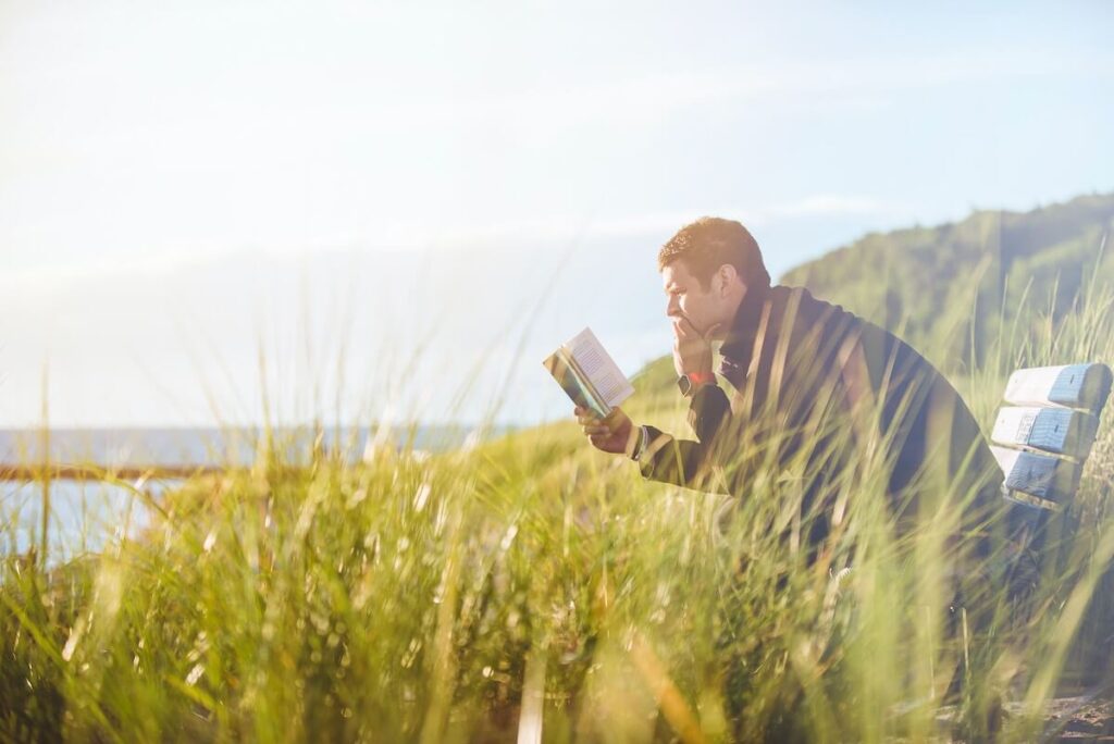 man reading on bench by waterfront