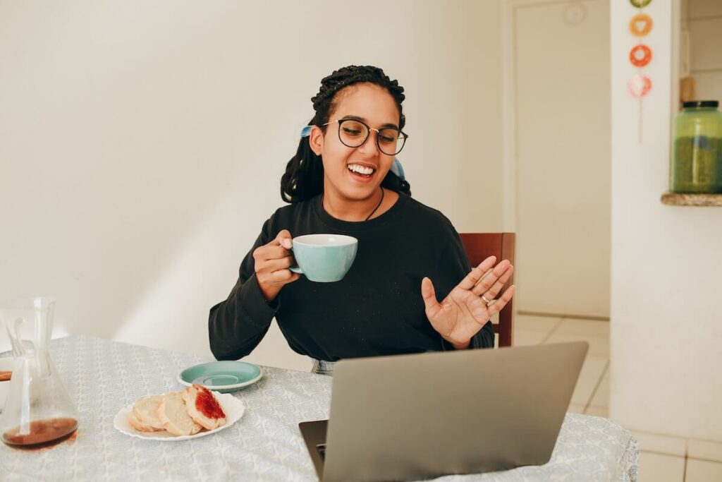 woman waves at computer screen while having breakfast