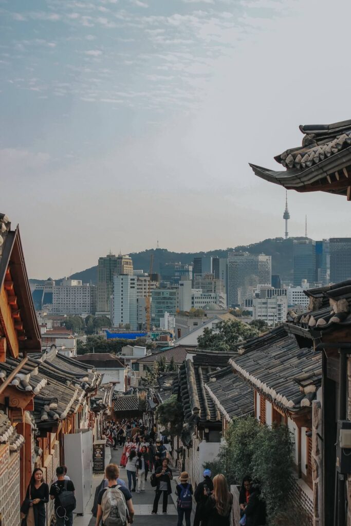 people walking along Bukchon Hanok Village with skyscrapers in the distance
