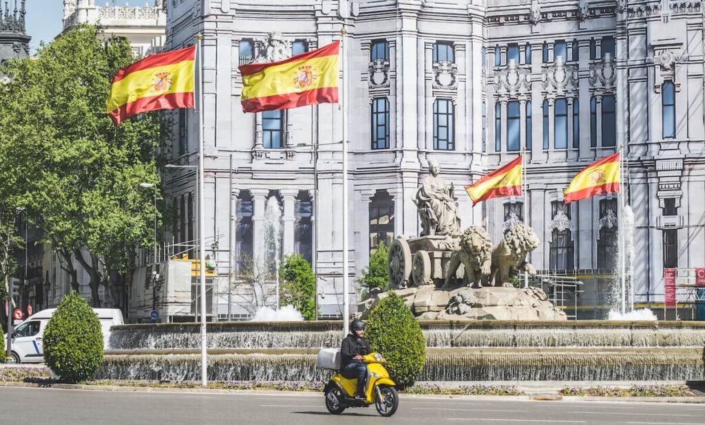 man driving yellow Vespa near a building in Spain