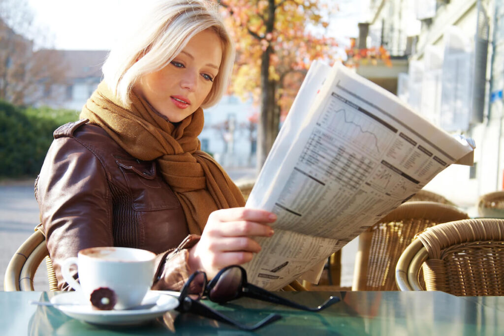 woman reading newspaper at cafe outdoor table