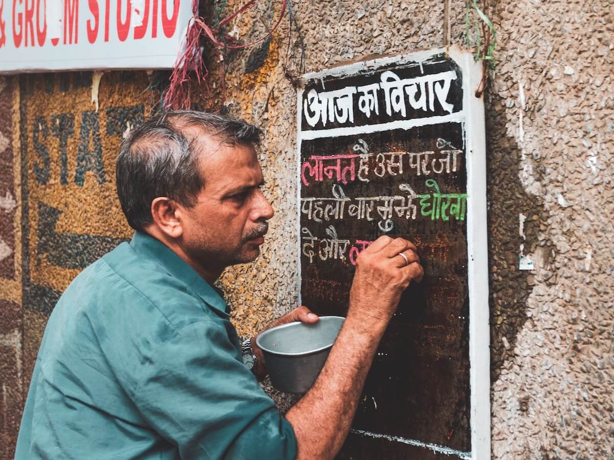 man writing Hindi characters on signboard