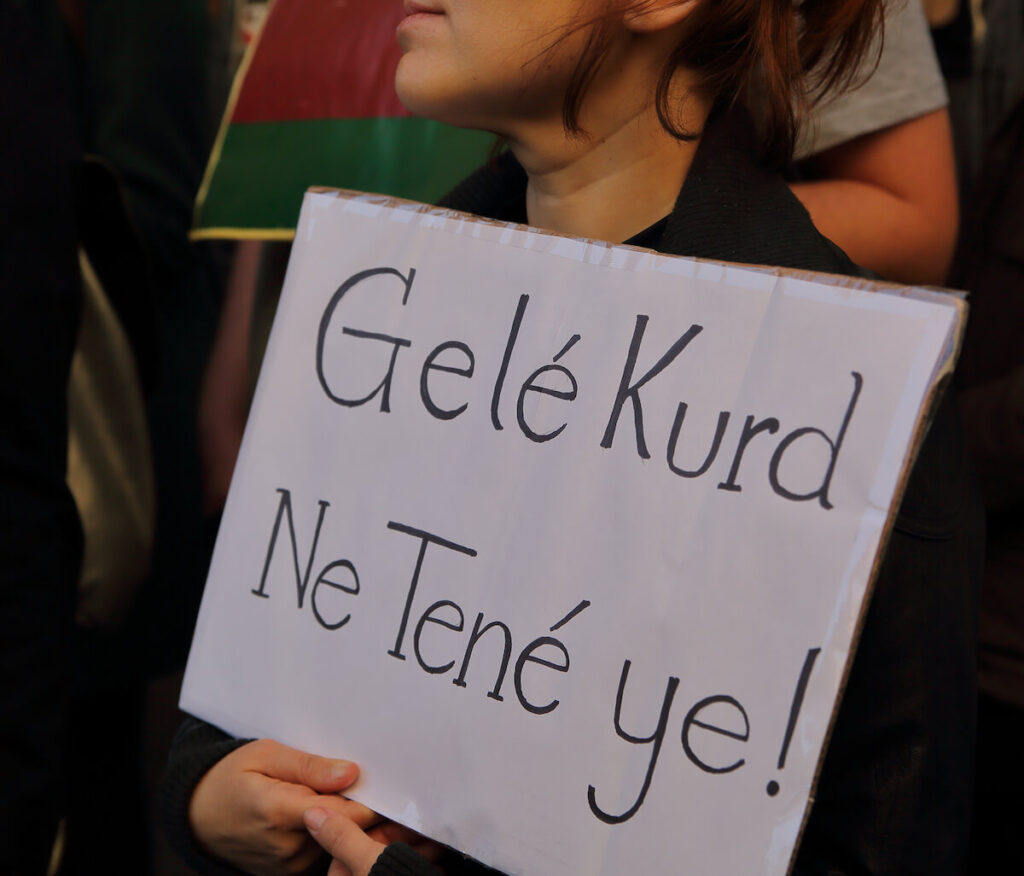 girl holds board with text SAVE KURDS in Kurdish language