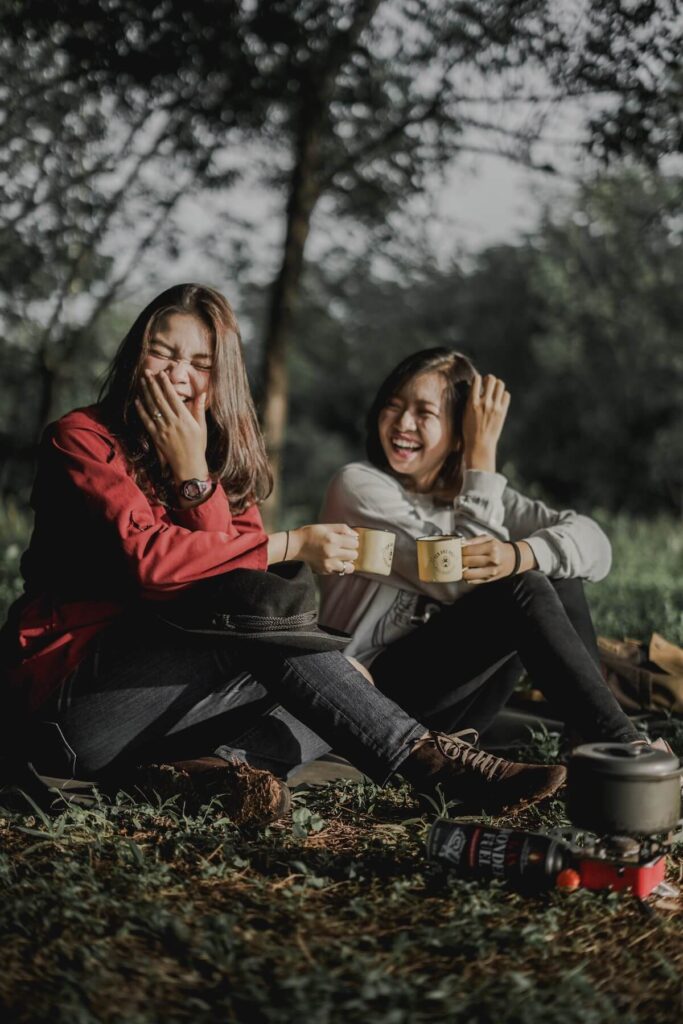 two women sitting on grass laughing