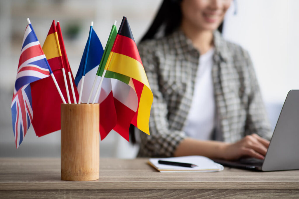 various country flags in a holder with woman typing in laptop in the background