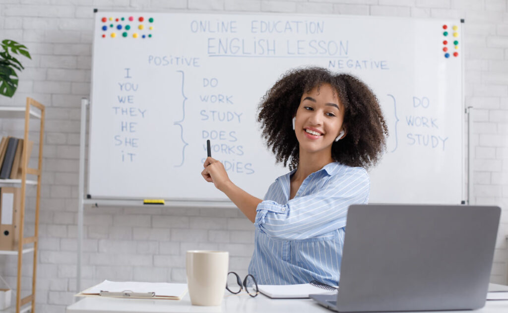 woman points to blackboard and explains rules of English to online student