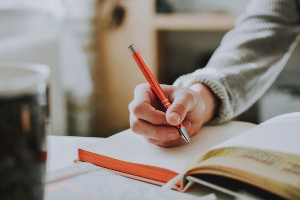person holding on red pen while writing on notebook