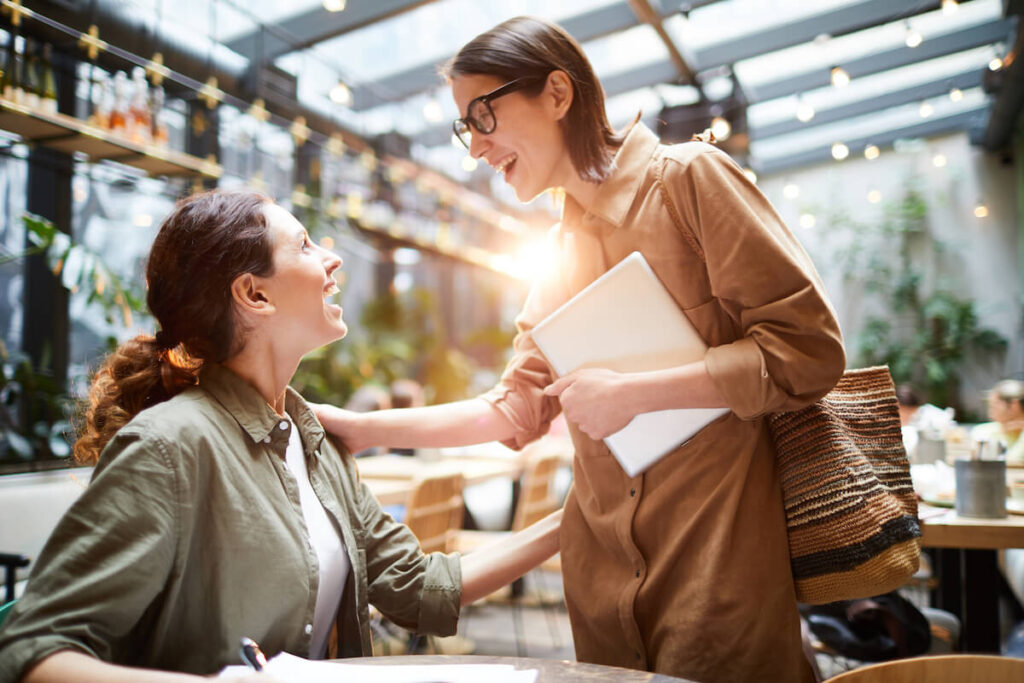 woman bumping into a friend and greeting her in a cafe