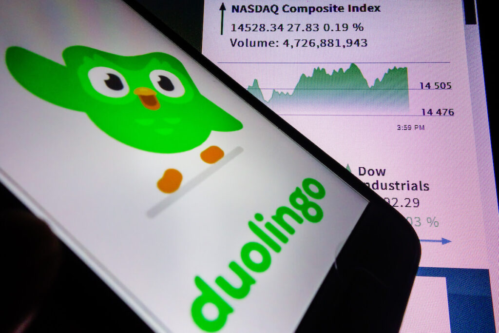 smartphone with Duolingo language app logo on screen and blurred background with Nasdaq stock exchange website