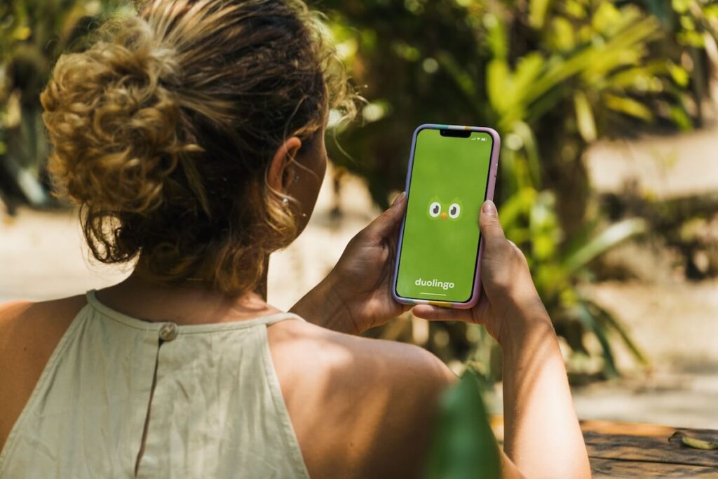 Woman in the park holding a smartphone with Duolingo language-learning app on the screen