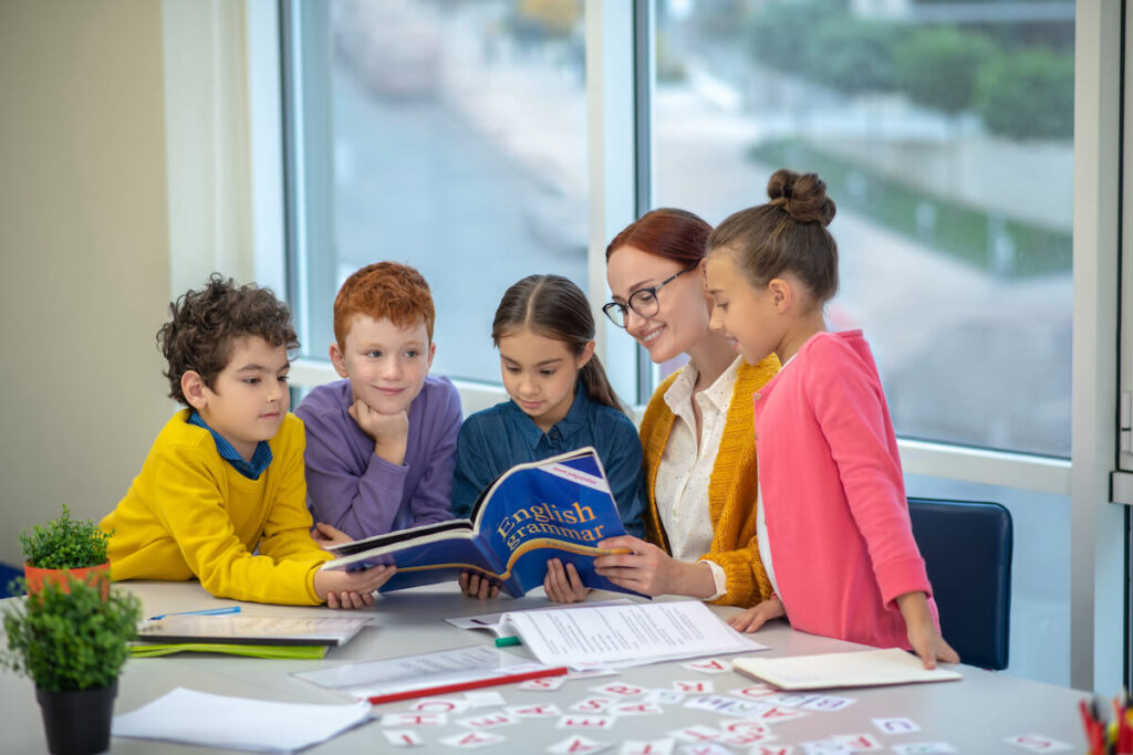 Children reading English grammar book with their teacher