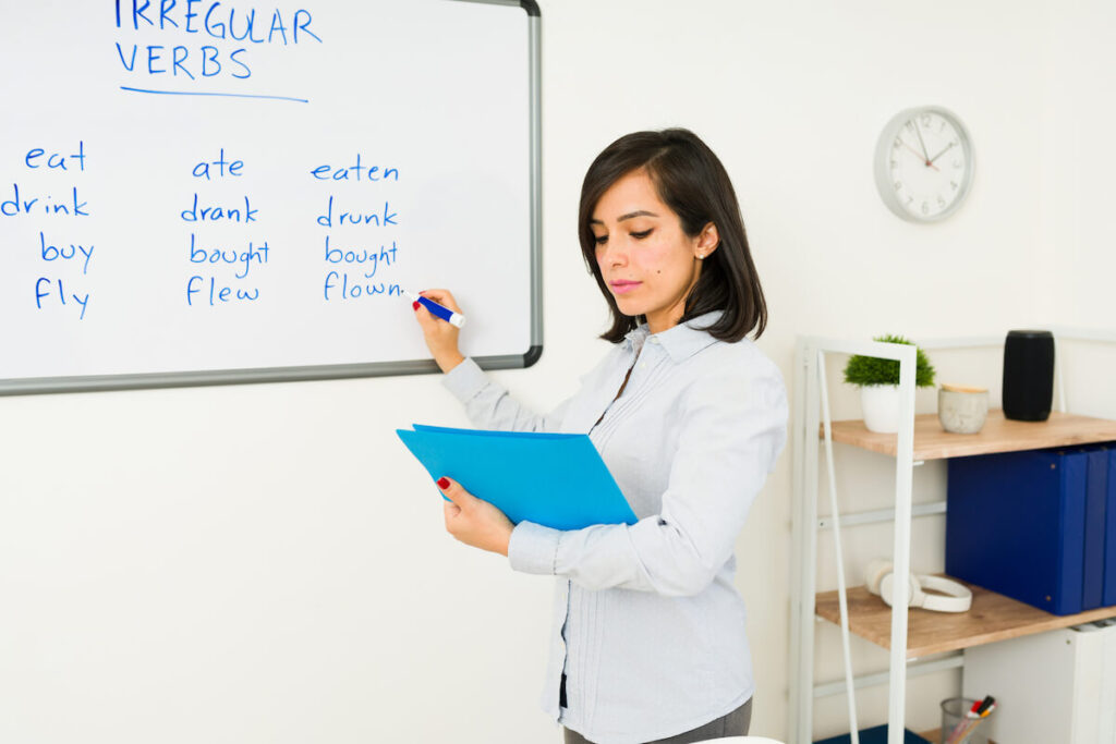 woman working as an English teacher writing verbs on the whiteboard