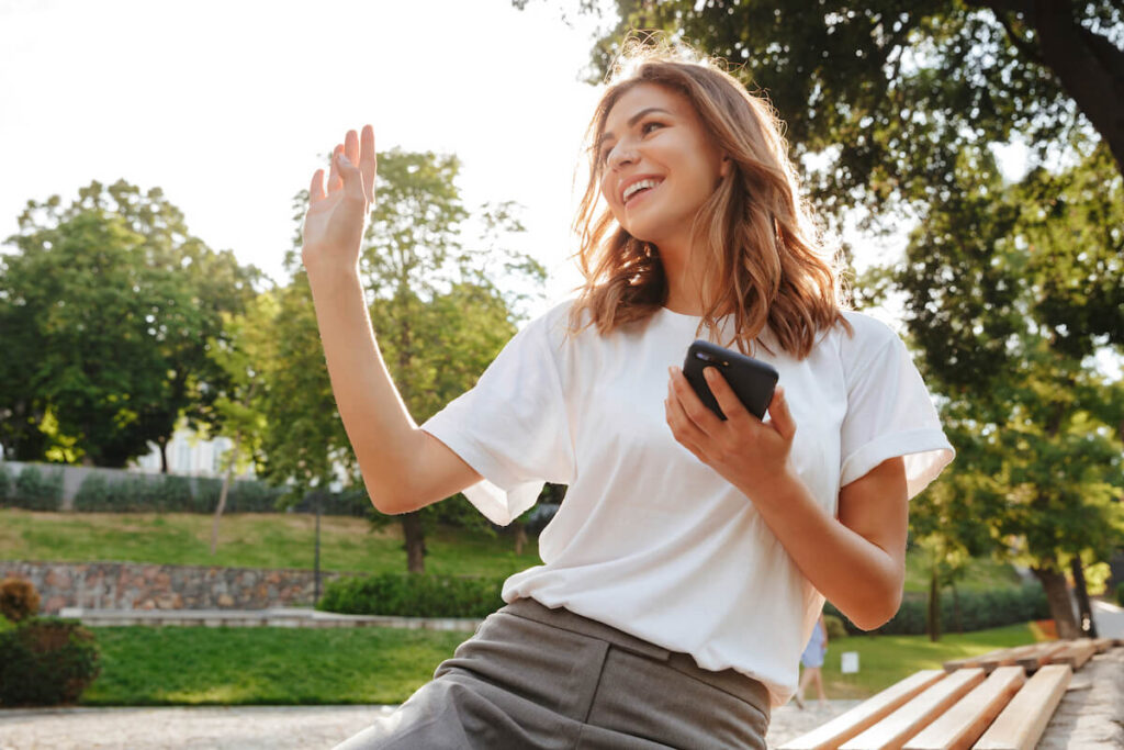 friendly woman sitting on bench in green park on summer day and waving hand aside saying hello 