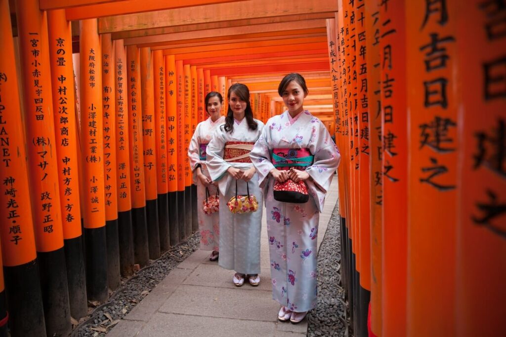 a group of women wearing kimono and standing next to each other in front of orange tori