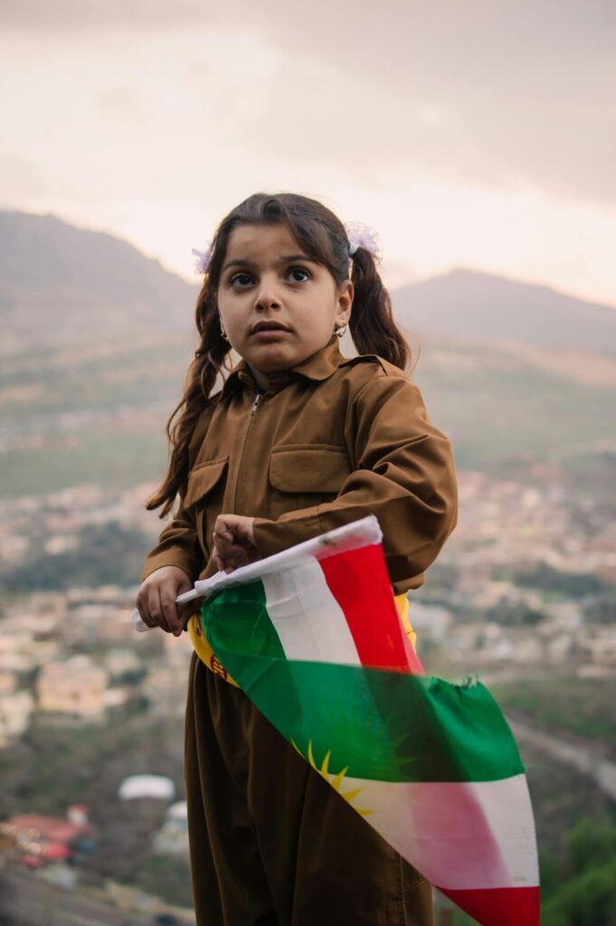 Kurdish child holding the flag of the Kurdistan Region while wearing Kurdish clothes in Akre