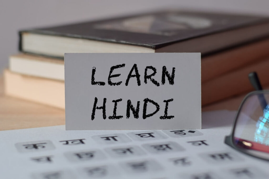 A card with the text LEARN HINDI on wooden desk with hindi alphabet letters