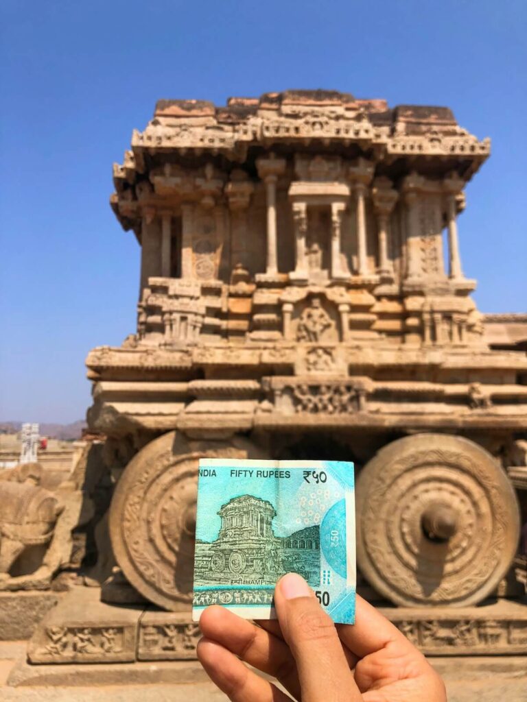 person holding a Rupee bill in front of a temple in Hampi, Karnataka, India