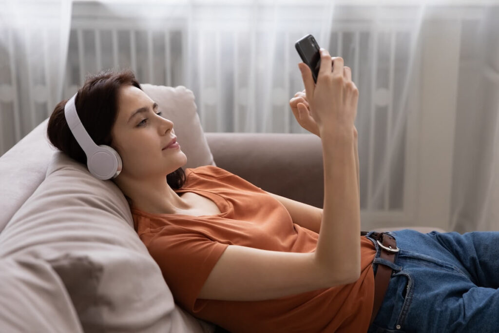 woman lying down while looking at phone and using headphones