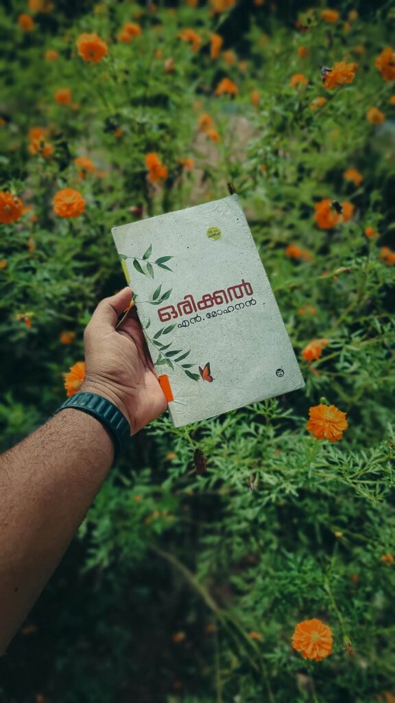 man holding a Malayalam book, with orange flowers in the background