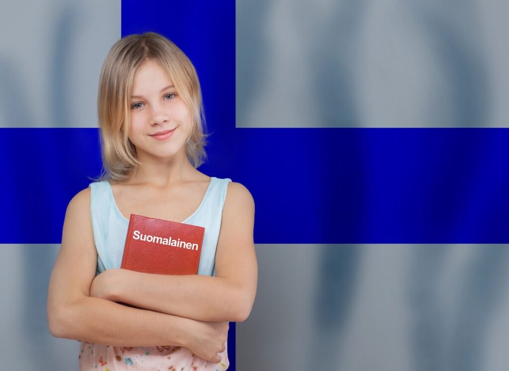 young woman holding a Finnish book, with Finnish flag in the background