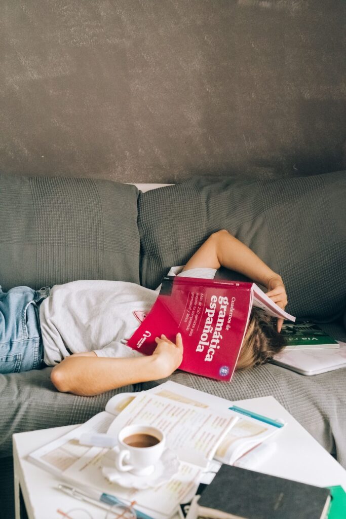 woman lying down in couch with Spanish grammar book covering face