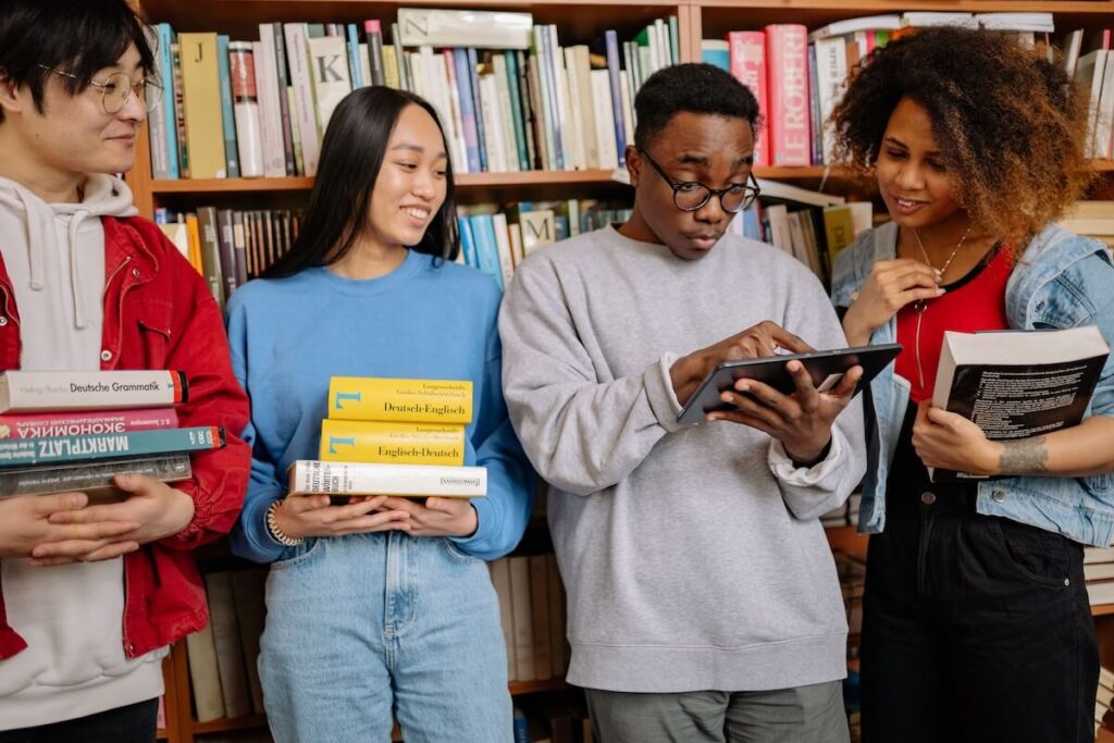 diverse students in library, holding language and marketing books